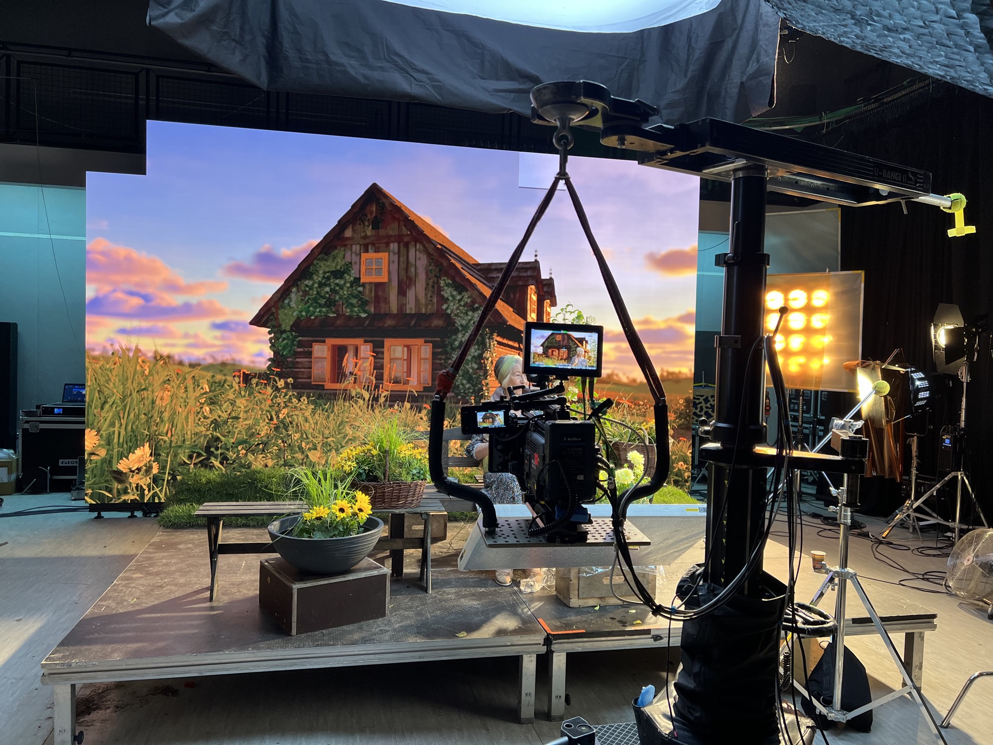Practical set built out in front of the LED wall - bench, flowers and turf continuing the cottage scene, camera on a crane